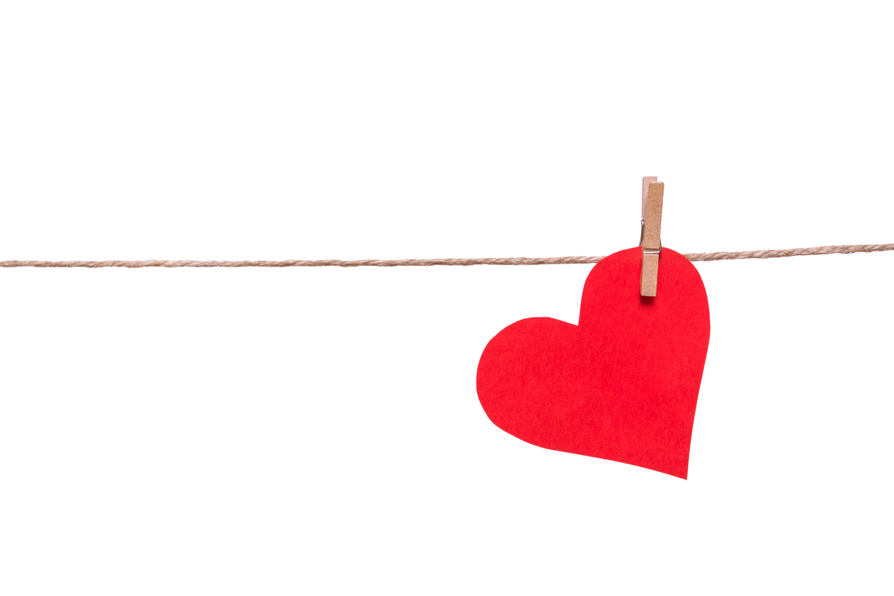 Red paper heart and clothespin on a rope isolated on white background.